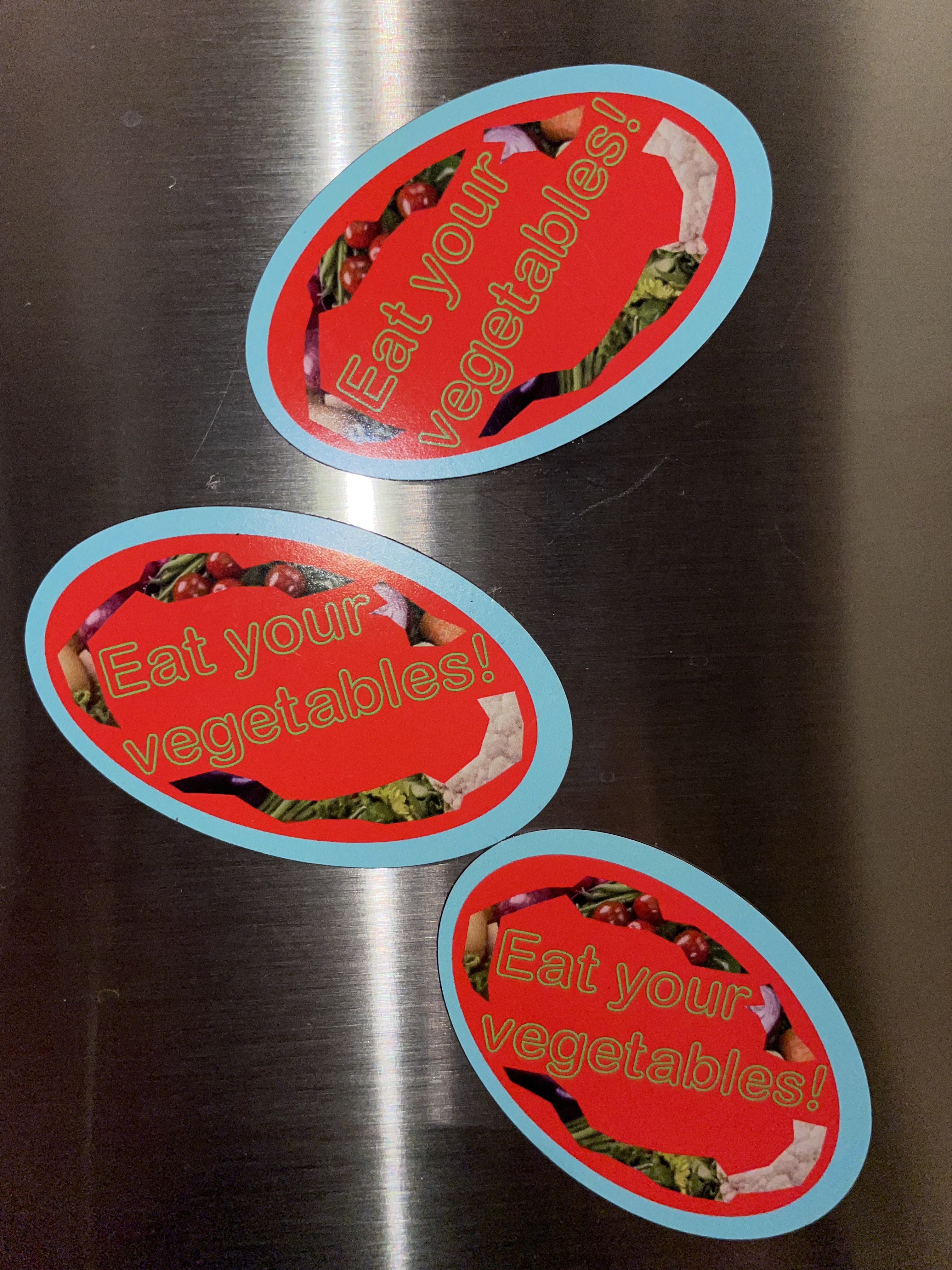 three red and turquoise magnets that read 'eat your vegetables' stuck on a fridge door